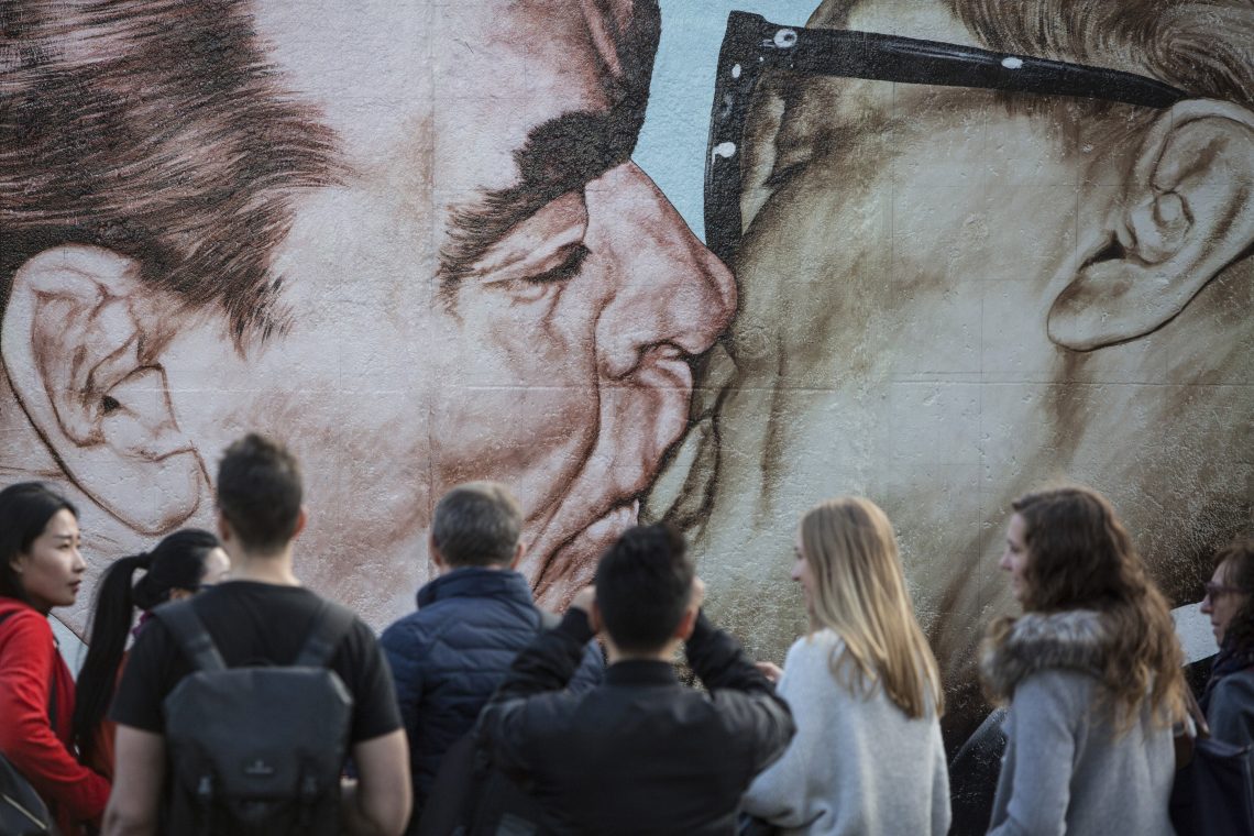 Foto von Touristen vor dem Sozialistischer Bruderkuss-Graffiti an der East Side Gallery in Berlin