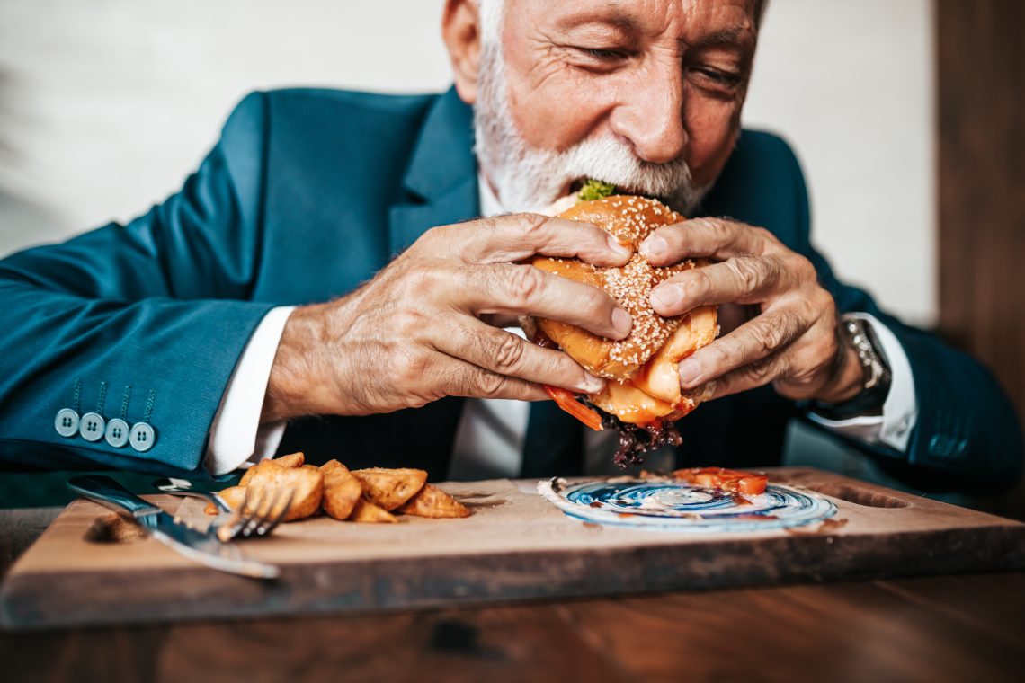 Älterer Herr im Anzug beißt in einen Burger