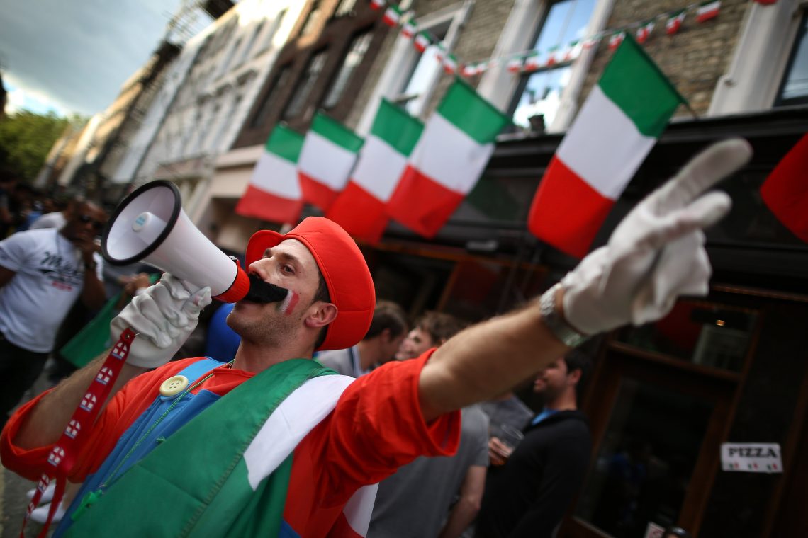 Eine Person die als Super Mario verkleidet ist und vor italienischen Fahnen steht