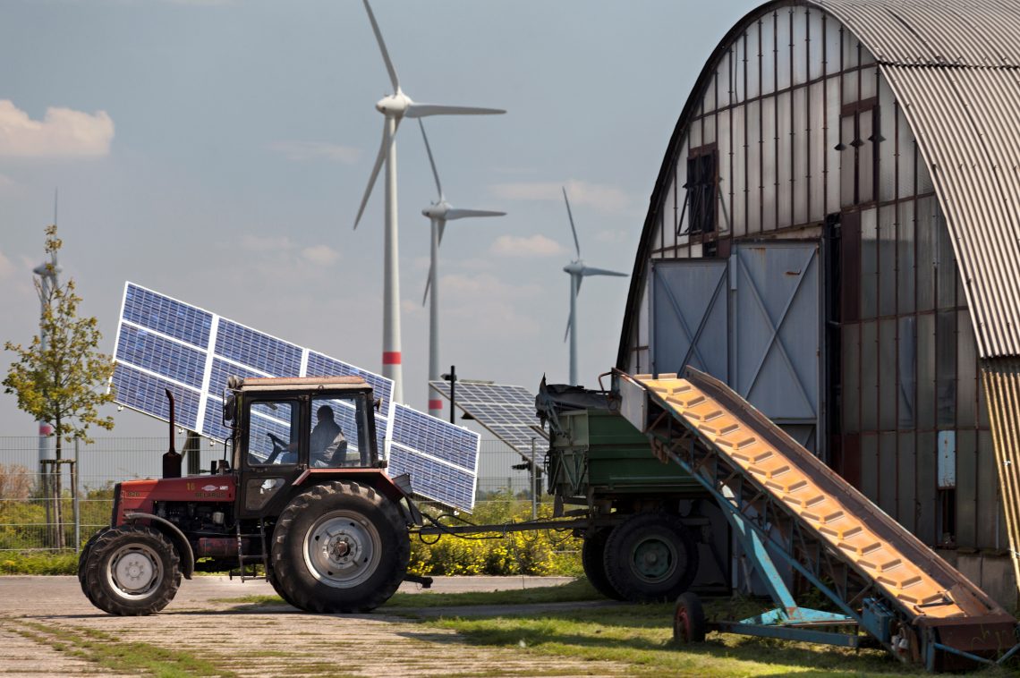 Ein Traktor in der energieautarken Gemeinde Feldheim vor einer Photovoltaikanlage und Windrädern