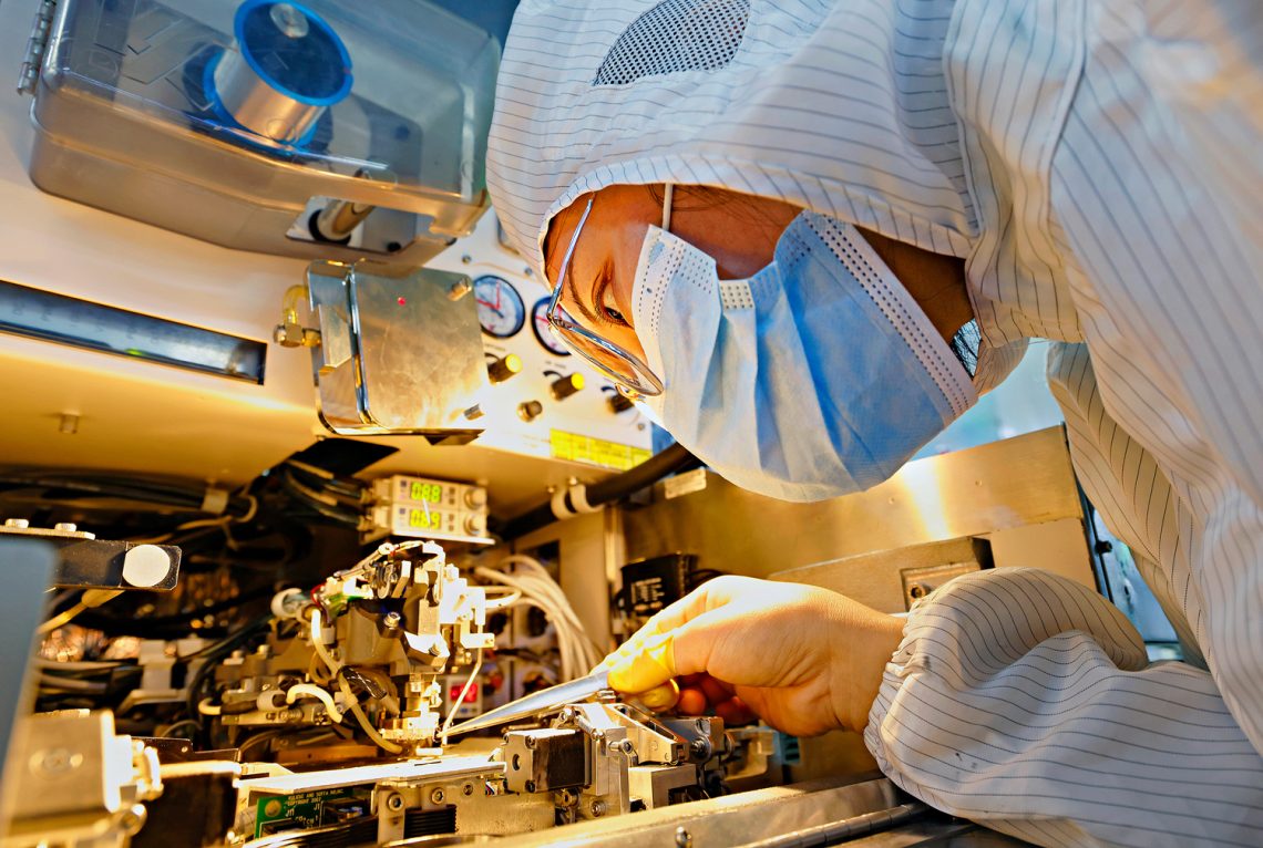Datendiebstahl: Foto einer Frau in Schutzkleidung, die an einer Maschine zur Herstellung von Computerchips arbeitet.