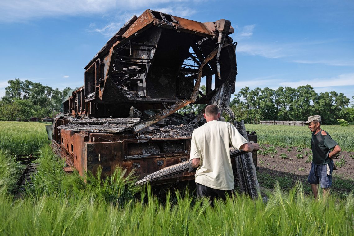 Männer durchsuchen ein ausgebranntes russisches Militärfahrzeug in einem Feld in der Ukraine, Juni 2022