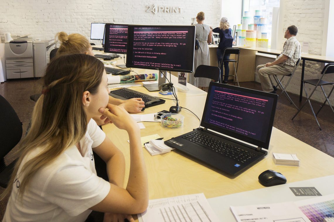 Ransomware: Mitarbeiterinnen in einem Geschäft blicken auf Laptop-Bildschirme, auf denen eine Erpressungsnachricht zu lesen ist.