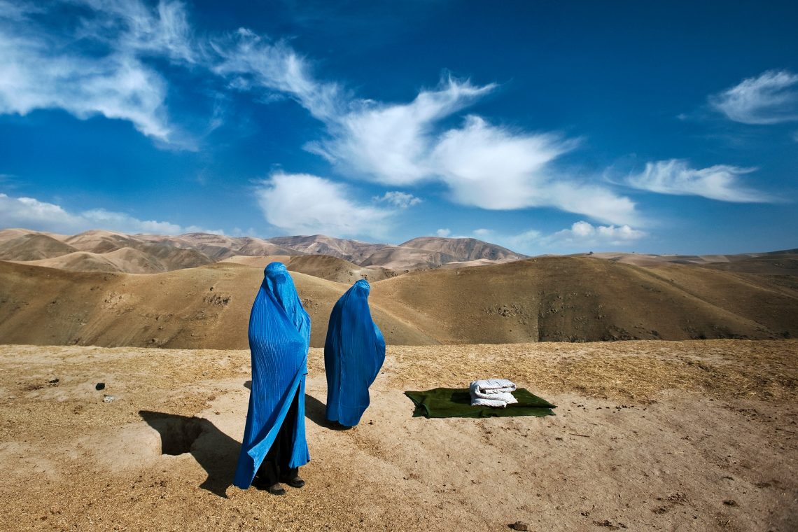 Foto von zwei Frauen mit Burka in Afghanistan. Im Hintergrund ist eine karge Hügellandschaft und sehr viel Himmel zu sehen.