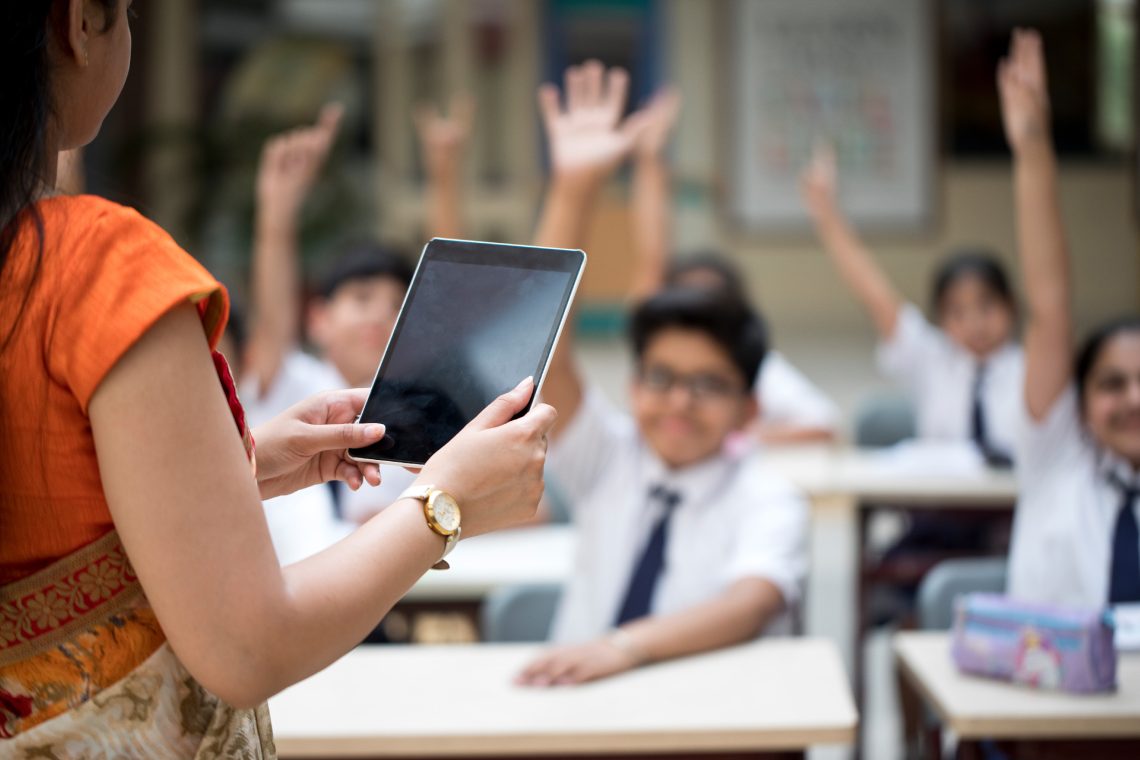 Indische Lehrerin mit Tablet in der Hand vor Schulklasse