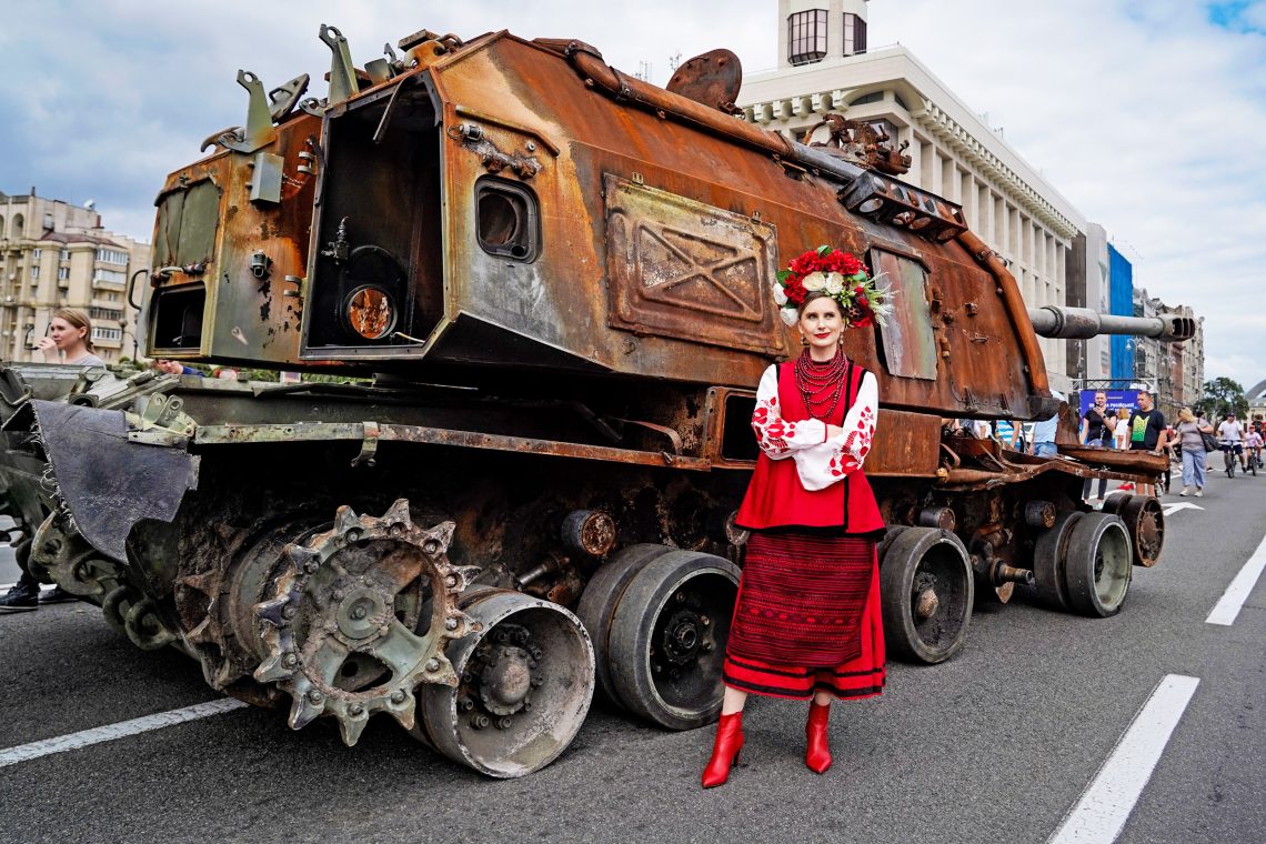 Ukrainerin in Nationaltracht vor einem ausgebrannten russischen Panzer in Kiew, 2022