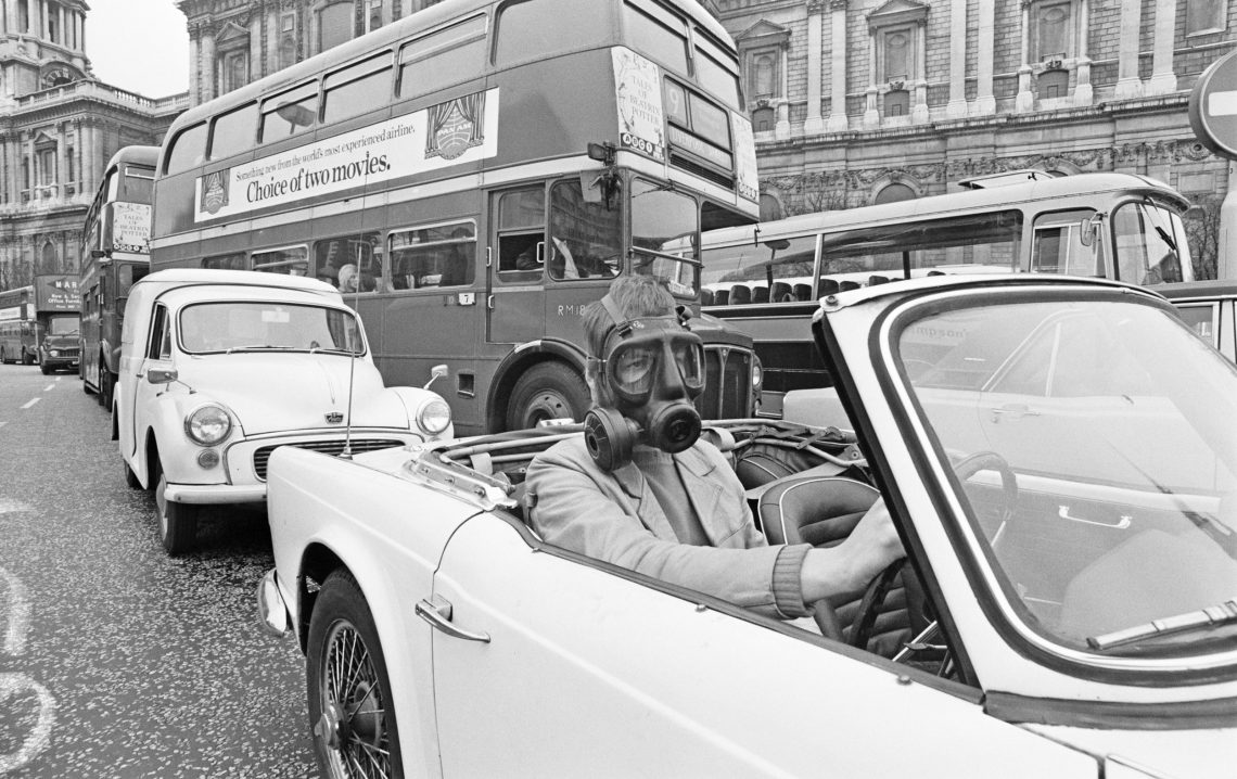 Ein Mann in einem Cabrio, der wegen der Abgasverschmutzung eine Gasmaske trägt, London 1971