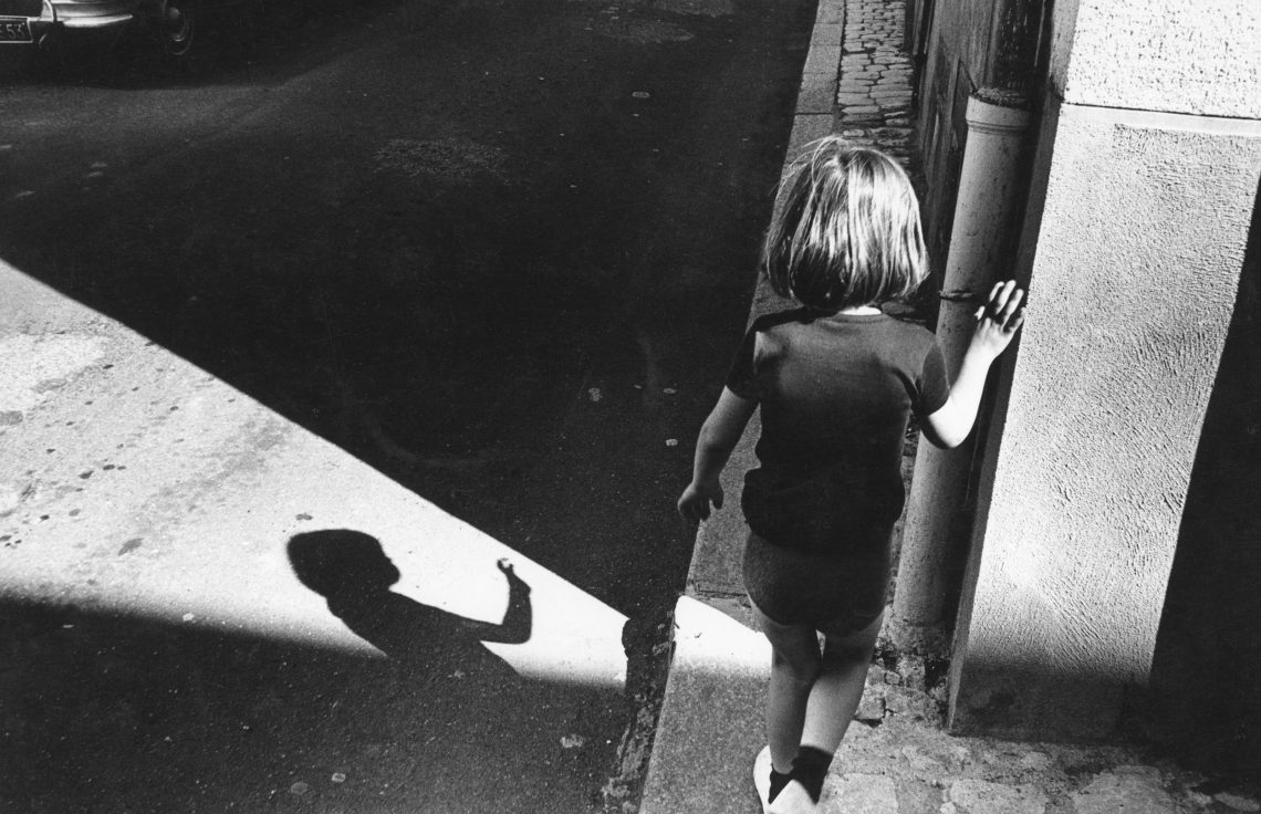 Schwarz-weiß Fotografie eines kleinen Mädchens das auf einem schmalen Bürgersteig eine Straße entlang geht.
