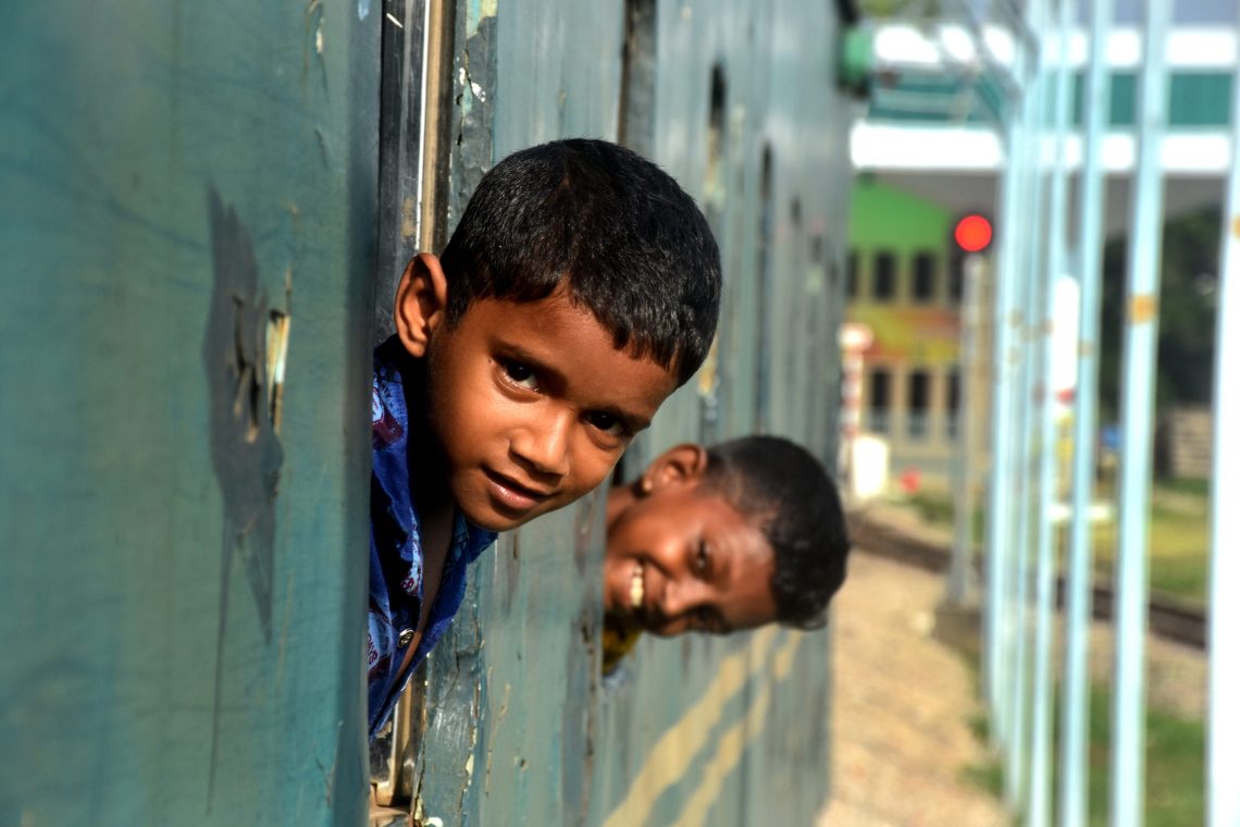 Foto von zwei Jungen, die lachend aus dem Fenster eines Zugwaggons blicken.