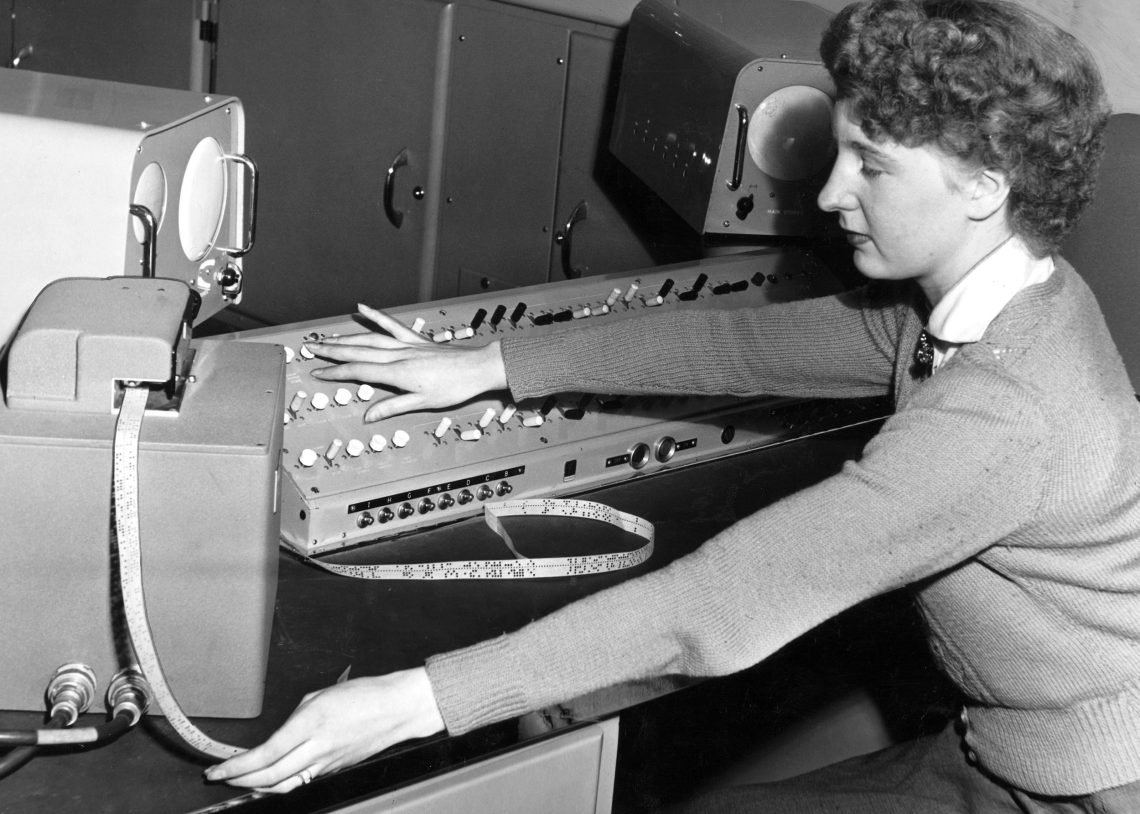 Eine junge Frau sitzt vor einer Maschine mit Lochkarten. Schwarzweiß Fotografie.