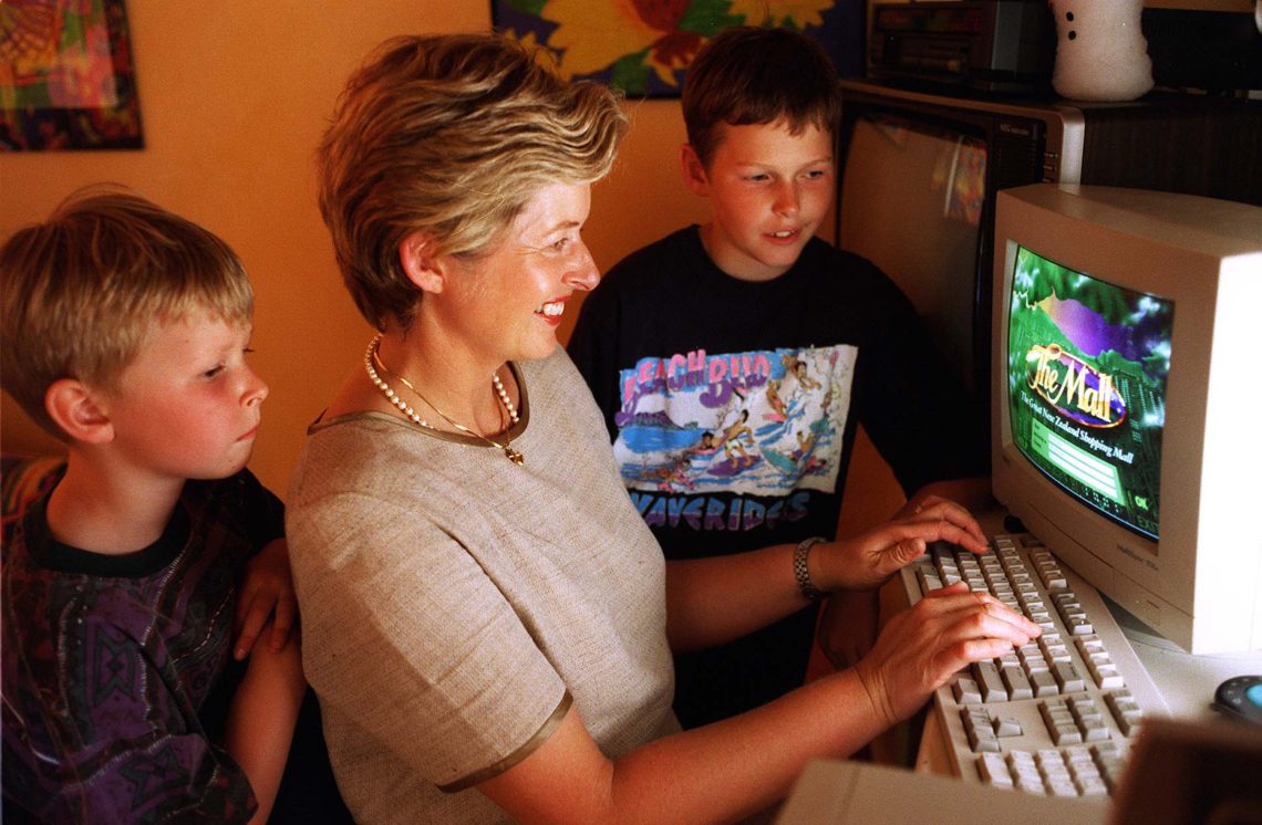 Eine Frau sitzt an einem Computer. Neben ihr stehen zwei Kinder, die ebenfalls auf den Computerbildschirm blicken. Auf dem Bildschirm sind die Warte "The Mll" zu lesen.