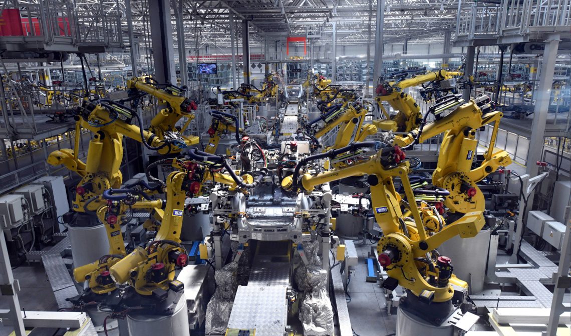 Foto einer Fabrikhalle, in der gelbe Roboter an einem Fließband arbeiten.