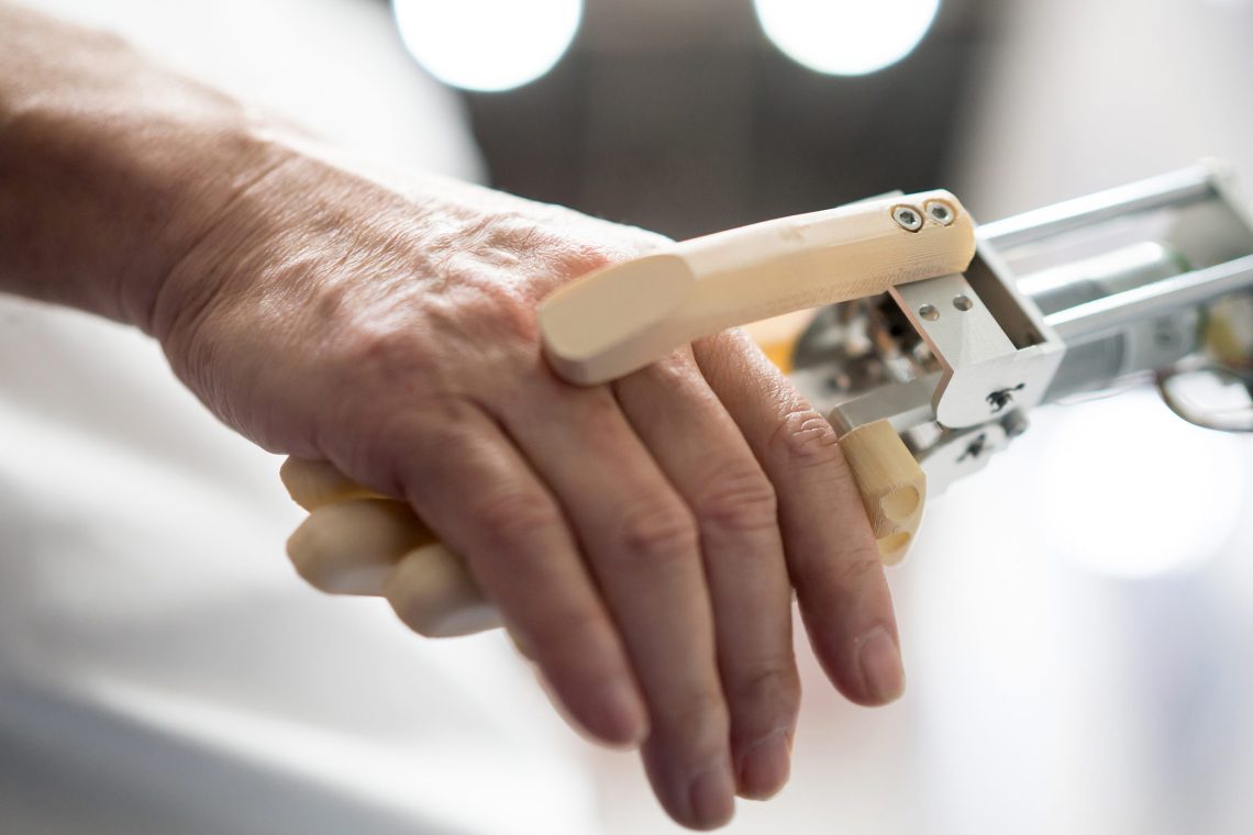 Foto einer Roboterhand mit Fingern aus hellem Plastik, die eine menschliche Hand hält.