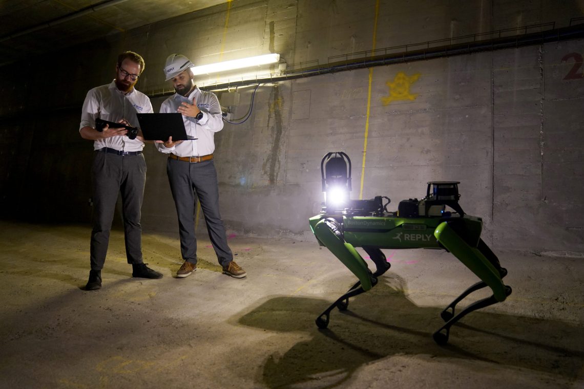 Zwei Männer in weißen Hemden, der eine mit Helm, stehen mit Laptop in der Hand in einem Tunnel. Neben ihnen ein grüner Roboter, dessen Gestallt an einen Hund oder eine Heuschrecke erinnert. Eine Maschinenethik gibt es für diesen Roboter noch nicht.