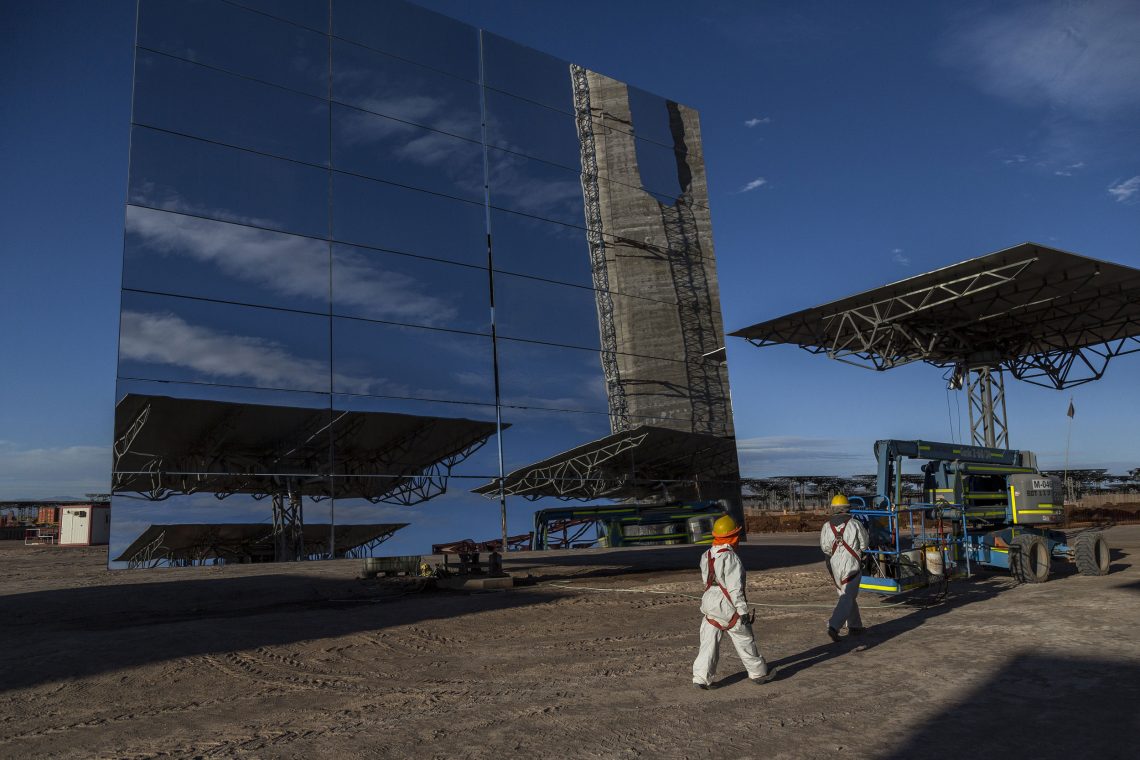 Energiewende in Chile: Fotos der riesigen Spiegel einer Solaranlage. Im Vordergrund gehen Arbeiter mit gelben Helmen.