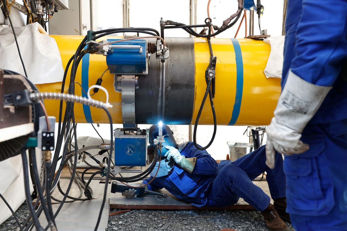 Energiewende in Deutschland: Foto von zwei Arbeitern in blauer Montur, die an einem gelben Rohr Schweißarbeiten verrichten.