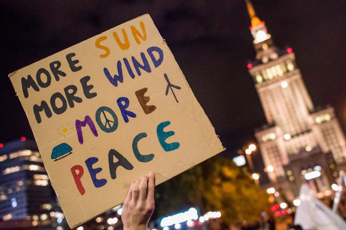 Foto einer Hand, die ein Schild hochhält auf dem steht "More Sun More Wind More Peace". Das Bild ist Teil eines Beitrags über die Energiewende.
