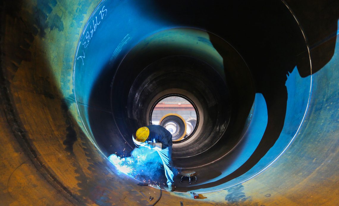 Ein Arbeiter mit einem gelben Schutzhelm steht in einer riesigen Metallröhre und schweißt.