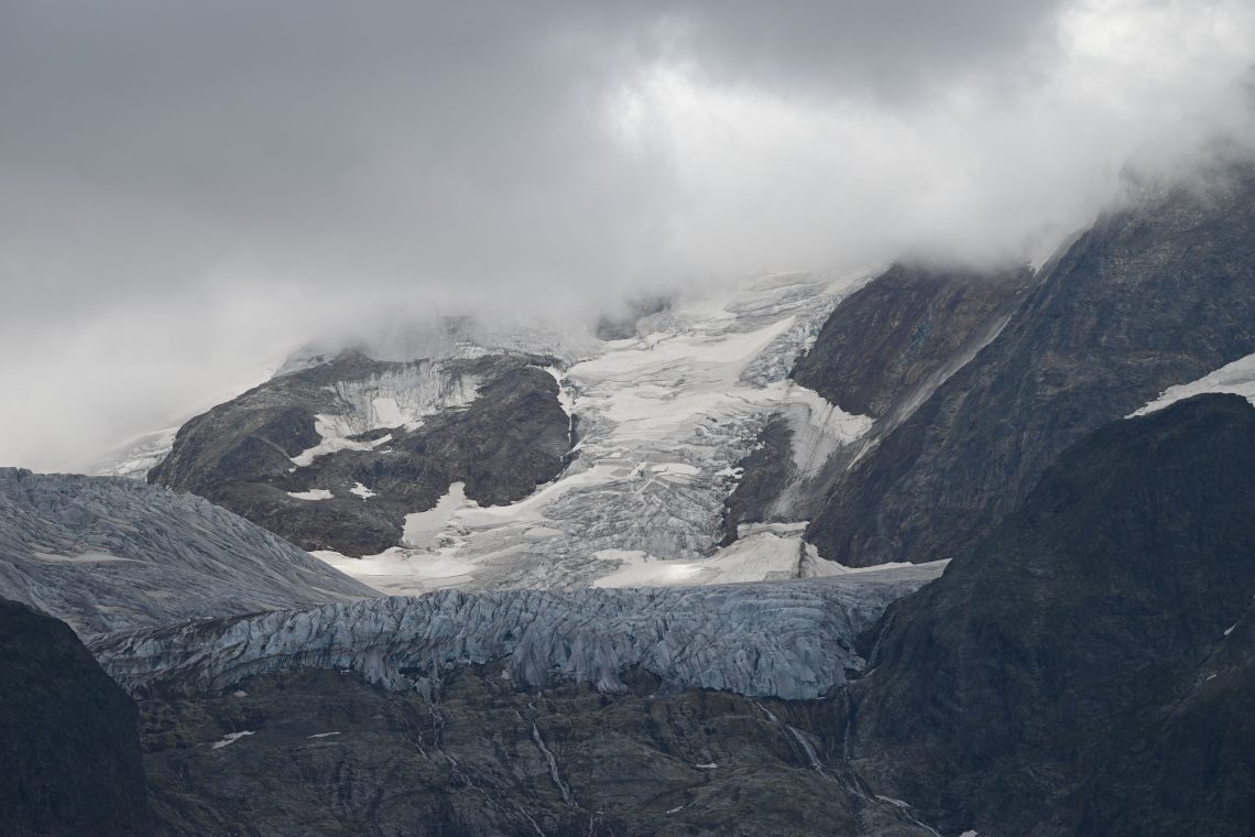 Ansicht eines Gletschers im Nebel auf felsigem Grund in einem Gebirge.
