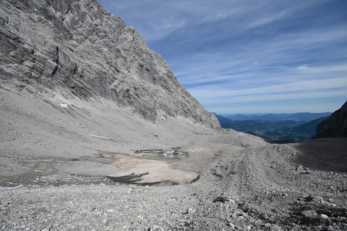Ein Geröllfeld mit einer winzig kleinen Eisfläche hoch oben auf einem Berg mit Blick in ein Tal.