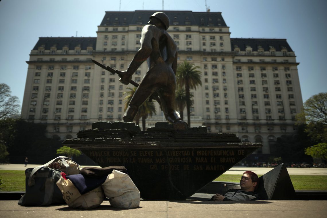 Foto eines Menschen, der vor einem großen Gebäude in einem Denkmal schläft, das Denkmal stellt einen Soldaten dar und hat eine Grube.
