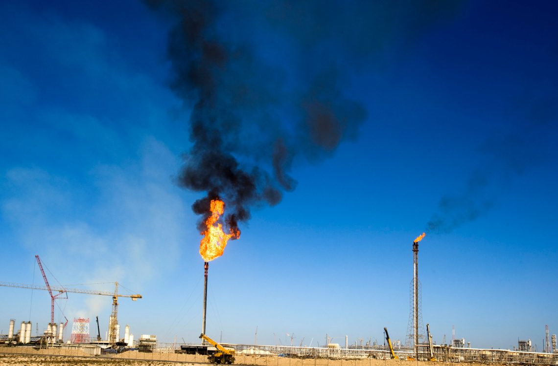 Foto von abfackelnden Erdgasleitungen mit Baukränen im Hintergrund. Das Bild steht für die Abhängigkeit des Westens von Katar.