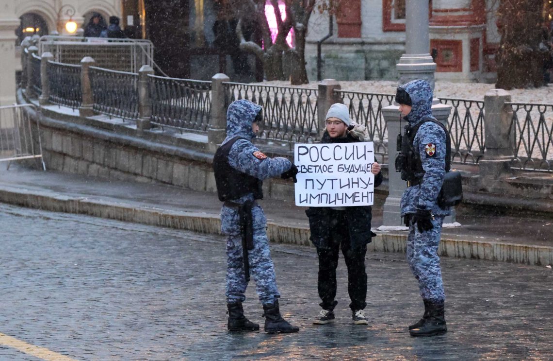 Denis, ein Demonstrant in Moskau, trägt ein Plakat mit der Aufschrift „Helle Zukunft für Russland, Amtsenthebung für Putin“ am 15. November 2022. Zwei Polisten in Tarnuniform flankieren ihn.