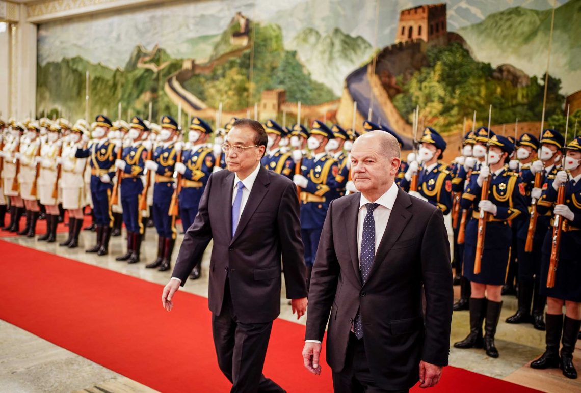 November 2022: Bundeskanzler Olaf Scholz wird von Premierminister Li Keqiang in der mit militärischen Ehren empfangen: hinter den Staatsmännern stehen Militärangehörige in Galauniform mit Gewehren und Schutzmasken vor einem Gemälde der chinesischen Mauer.