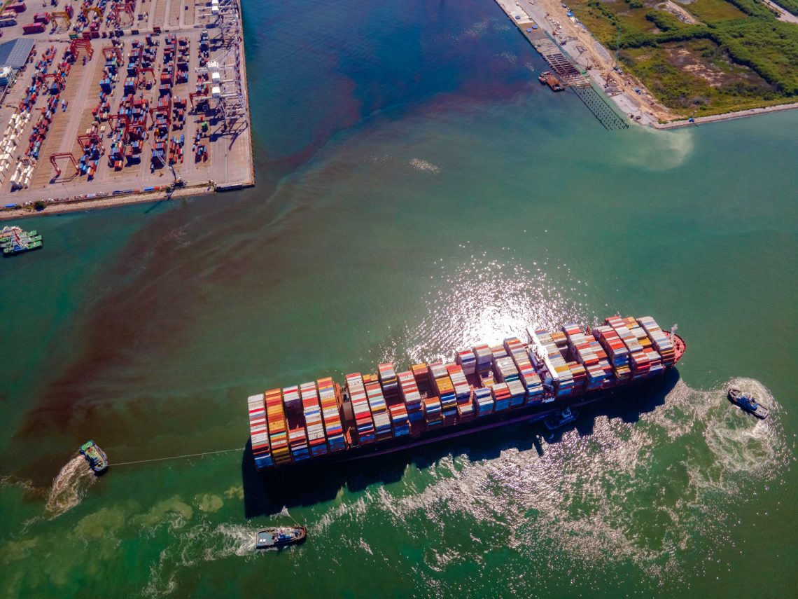 Luftaufnahme eines voll beladenen Containerschiffs, das von Schleppern in Thailands größten Hafen Laem Chabang geführt wird.