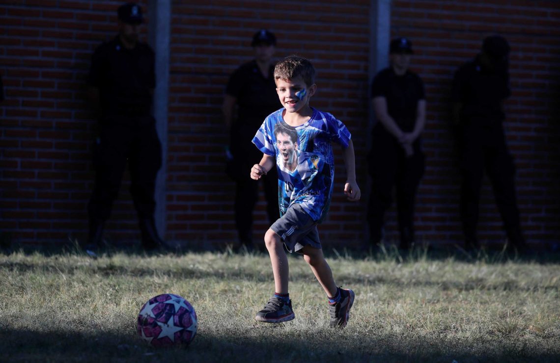 Ein Junge im T-Shirt mit dem Konterfei von Lionel Messi, spielt Fußball, während er auf die Ankunft der WM-Sieger in Buenos Aires wartet.