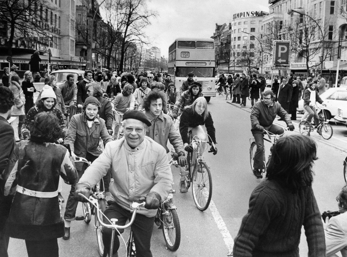 Ein Gruppe von Radfahrern fährt auf einer großen Straße mit einem Bus in der Mitte. Das Foto illustriert einen Beitrag über Zinsen und Inflation.