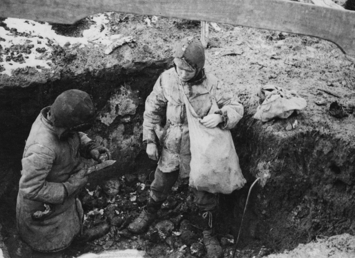 Schwarzweiß Foto von zwei Jungen mit Stoffsäcken die in einer Grube stehen und Kartoffeln von Erde reinigen. Das Bild zeigt die Folgen des Holodomor, der international aber nicht als Völkermord gilt.