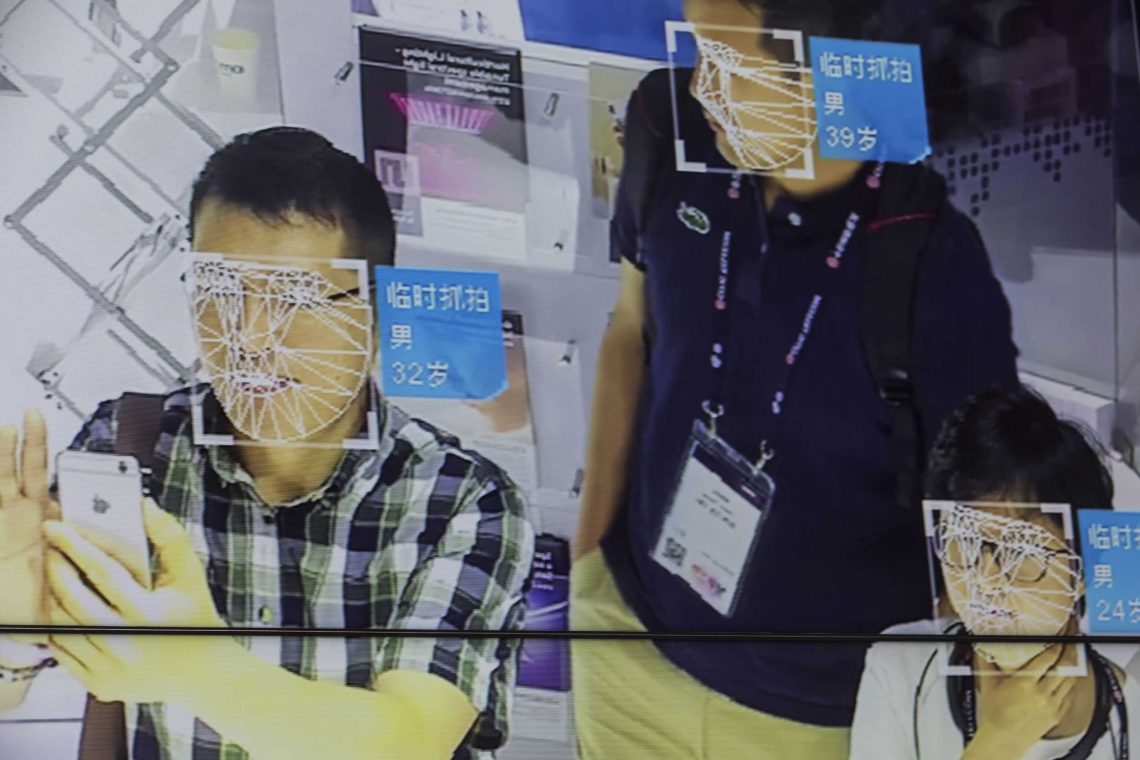 Ein Bildschirm zeigt eine Gesichtserkennungstechnologie auf der einer Messe in Shanghai 2019. Geometrische Linien ziehen sich über das Gesicht einer Testperson, die vor einer Kamera steht.