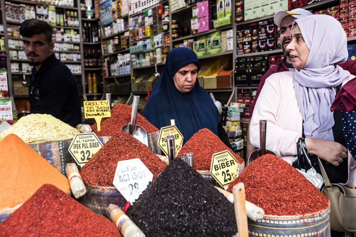 Einkäufer in einem Lebensmittelgeschäft in Istanbul stehen vor bunten aufgehäuften Gewürzen.