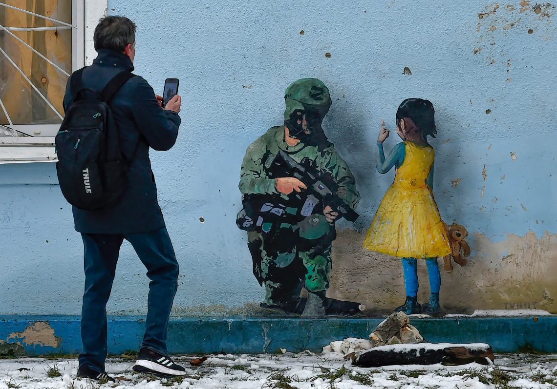 Ein Straßenbild im ukrainischen Ort Irpin des Künstlers Tvboy von einem Mädchen, gekleidet in den Nationalfarben, das einem Soldaten in Kampfmontur die Hand auf die Schulter legt.