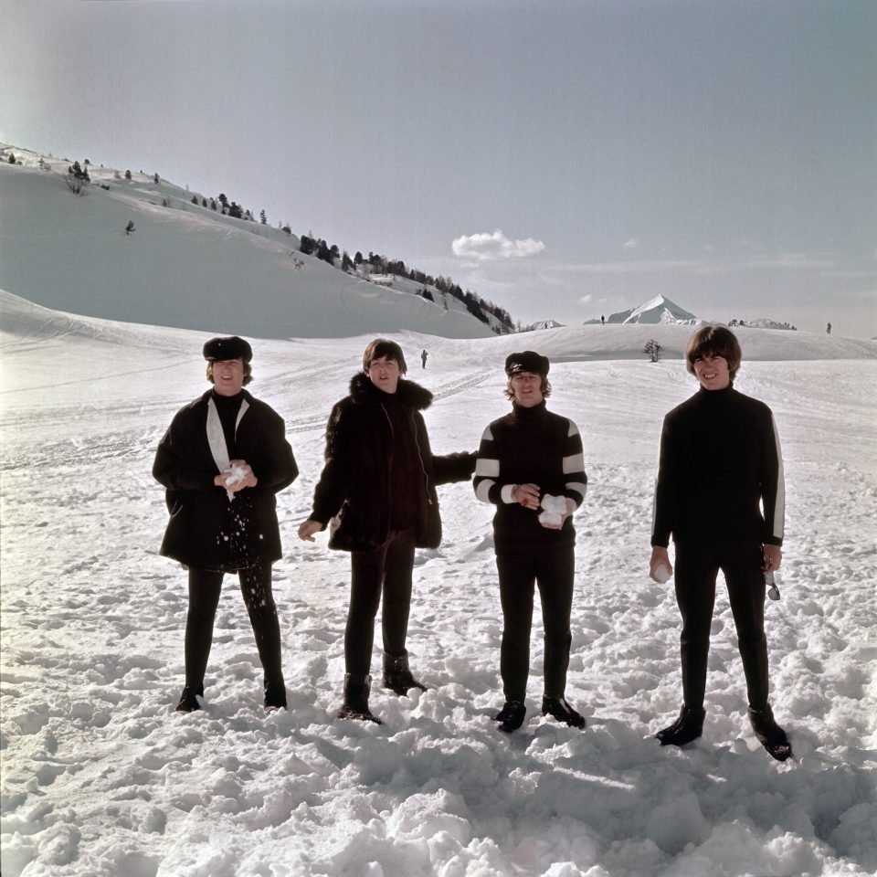 Die Beatles posieren in einer mit hohem Schnee bedeckten Gebirgslandschaft. Es ist ein Bild mit starken Kontrasten zwischen schwarz und weiß, aber eine Farbaufnahme. 
