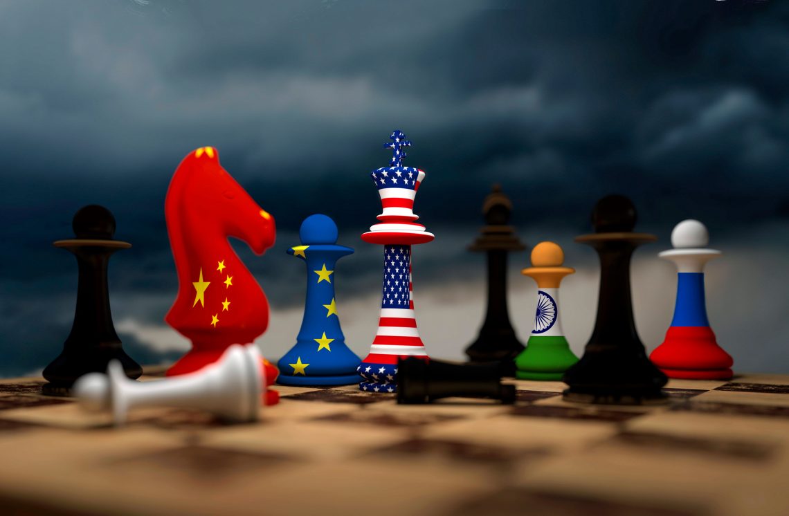 Einige Schachfiguren in den Farben nationaler Flaggen auf eiem Spielbrett: Der Springer (China) hält die USA (König) in Schach, drei Bauern (EU, Indien und Russland) stehen dahinter.