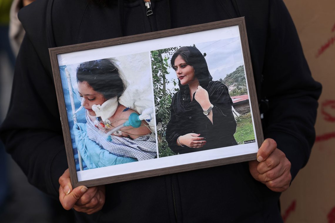 Eine Frau hält einen Bilderrahmen mit zwei Fotos, die eine junge Frau zeigen. Auf dem einen Foto ist sie verwundet, auf dem anderen Foto steht sie lächelnd in einem Garten.