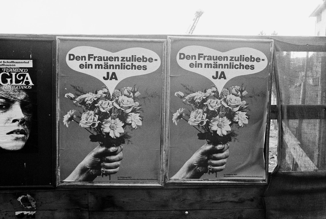 Foto von zwei Wahlplakaten mit identischem Motiv. Auf dem Platat steht: Den Frauen zuliebe - ein männliches Ja. Eine Frauenhand hält einen Blumenstrauß, darüber ein Herz mit dem Slogan. Das Bild gehört zu einem eitrag über den Wohlstand in der Schweiz und das Mitbestimmungsrecht der Bürger.