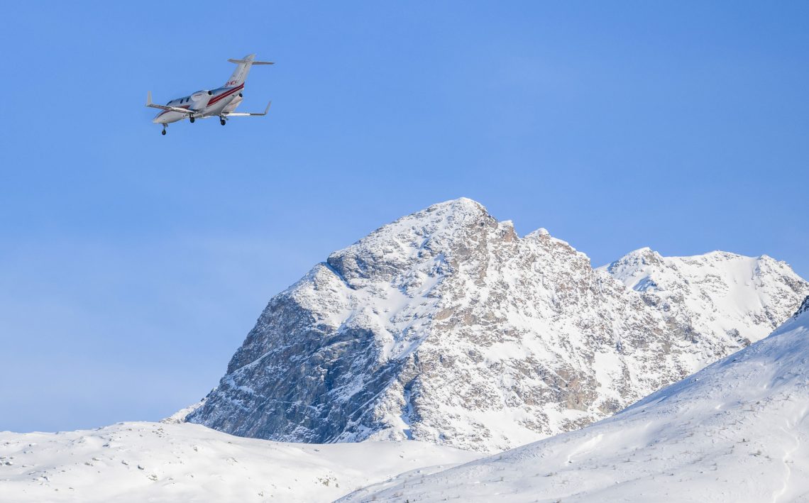 Foto eines kleinen Propellerflugzeugs über schneebecktem Gebirge bei blauem Himmel. Das Bild ist Teil eines Beitrags über die Wirtschaft und den Wohlstand in der Schweiz.