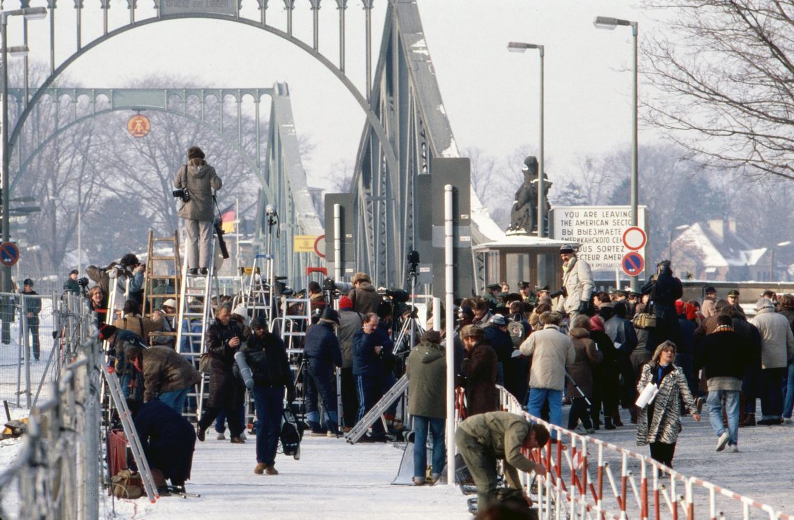 Foto einer Menschenmenge auf einer Brücke verschneiten Brücke im Winter. Viele sind Fotografen und haben Leitern mitgebracht, sie scheinen auf etwas zu warten. Am Rand stehen Schaulustige.