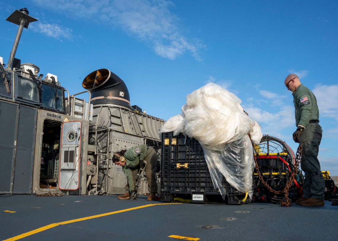 Foto von militärischem Personal, das einen großen Plastikhaufen in eine Kiste packt. Das Bild illustriert einen Beitrag über Spionage, bei dem Plastikhaufen handelt es sich um den chinesischen Spionageballon. 