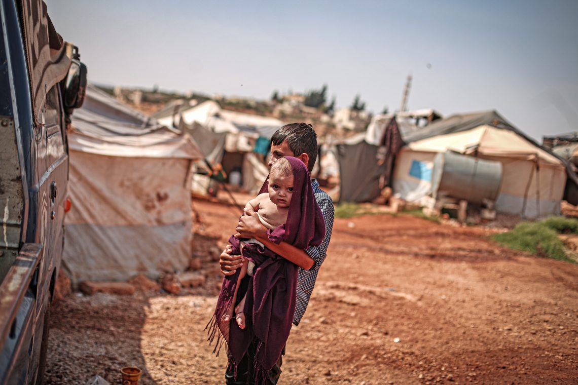 Syrischer Junge mit Baby auf dem Arm im Flüchtlingslager Idlib, Syrien, 2020