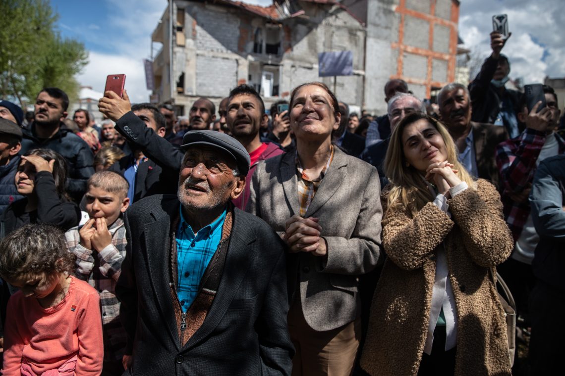 Anhänger des Präsidentschaftskandidaten des größten Oppositionsbündnisses Kemal Kilicdaroglu stehen andächtig bei einer Kundgebung im April in Adiyaman. Im Hintergrund sieht man ein vom Erdbeben beschädigtes Gebäude.