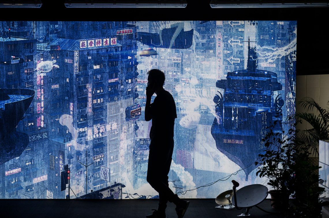 Hongkong, 2020: Ein Mann geht an einer futuristischen Stadtlandschaft vorbei, die Teil einer Cyberpunk-Ausstellung ist.