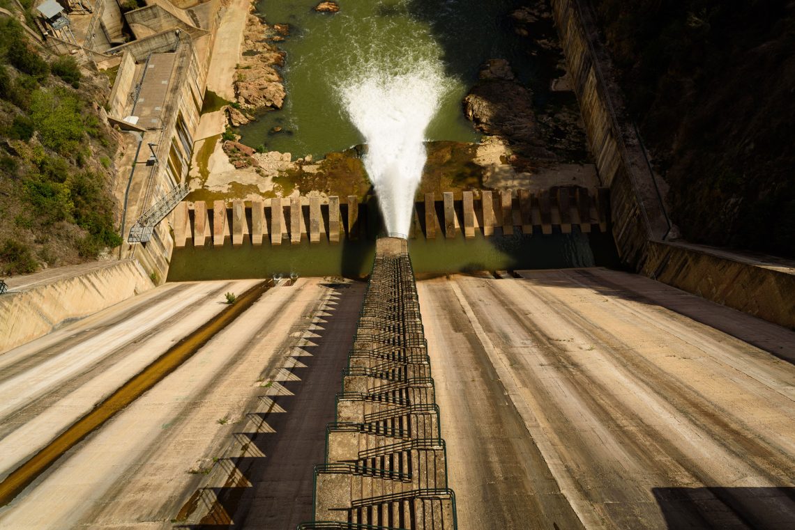 Foto von Oben eine Staumauer hinunter. Unten schießt Wasser in ein Reservoir. Das Bild illustriert einen Beitrag über Maßnahmen in Folge des Klimawandels und die These der Klimadiktatur.