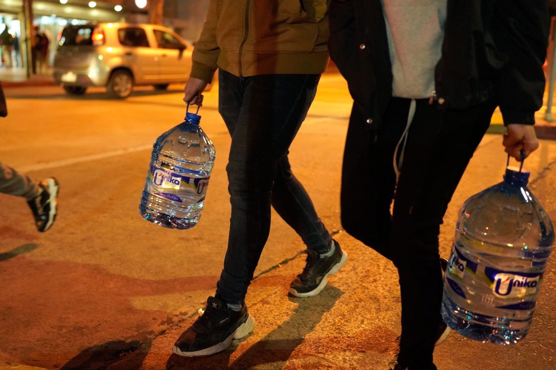 Foto von zwei Menschen, die Wasser in Plastikflaschen tragen. Das Bild illustriert einen Beitrag über Maßnahmen in Folge des Klimawandels und die These der Klimadiktatur.