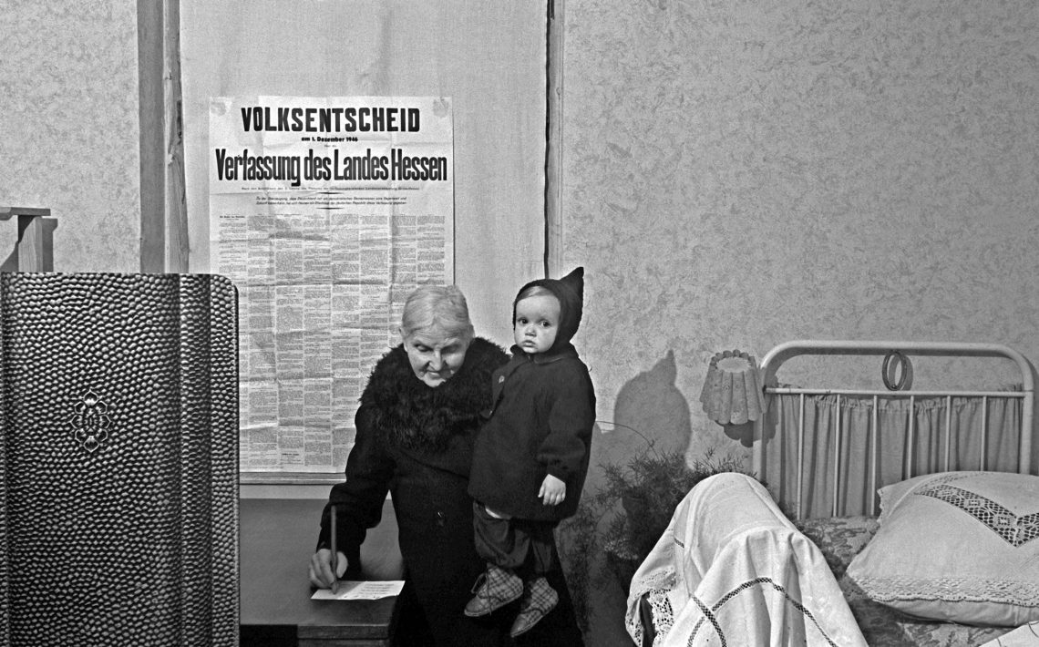 Hessen, 1946: Eine 90-jährige Frau mit ihrem Ur-Enkel auf dem Arm gibt bei der Volksabstimmung über die Hessische Verfassung ihre Stimme für die junge Demokratie ab.
