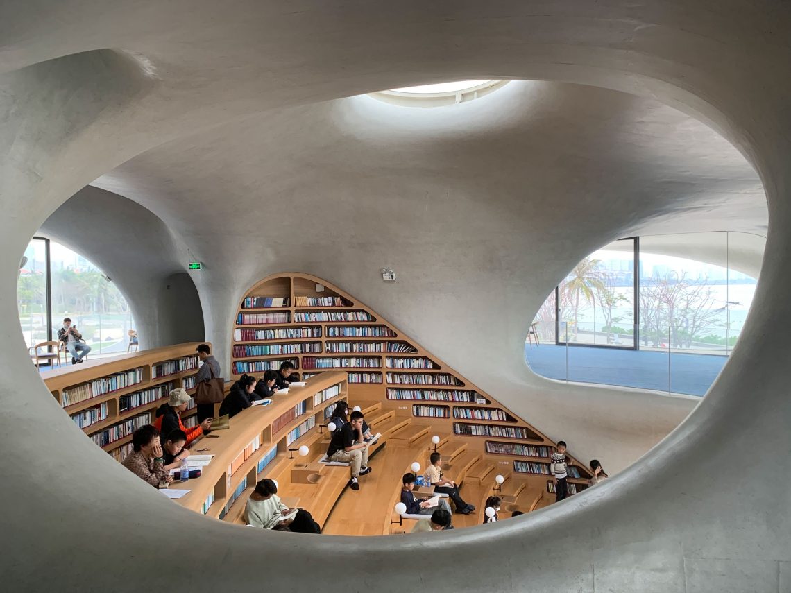 Ansicht eines Lesesaals in einem organisch geformten Gebäude mit sehr großen Fenstern. Das Bild illustriert einen Beitrag über Bibliotheken und die Geschichte des Lesesaals.