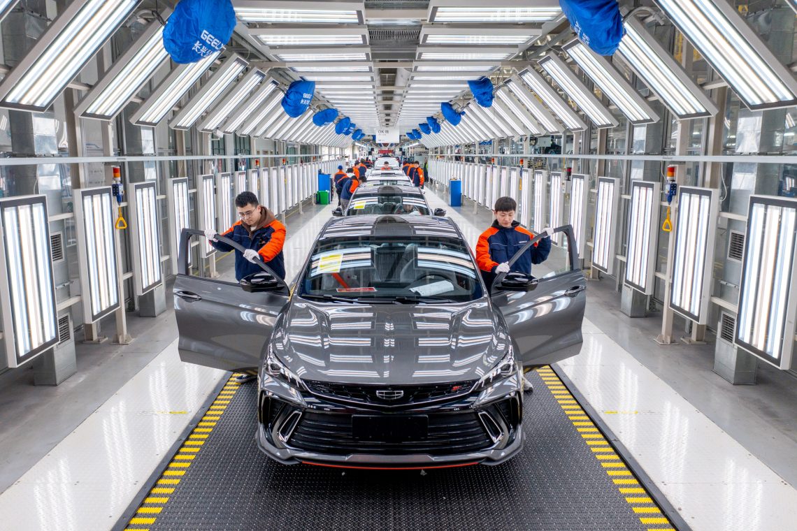 Zwei Mitarbeiter stehen an einem Förderband neben einem fast fertig montierten Auto des chinesisches Herstellers Geely.